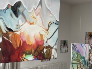 Abstrakte Gemälde mit wirbelnden Formen und leuchtenden Farben sind auf hängenden Leinwänden in einem weißwandigen Galerieraum ausgestellt.