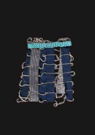 Ein handgewebtes Textilstück mit vertikalen und horizontalen blauen und grauen Stoffstreifen, locker gewebt mit ausgefransten Rändern, und einer türkisfarbenen gehäkelten oberen Bordüre, vor schwarzem Hintergrund.