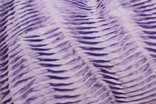 Nahaufnahme eines hellvioletten Stoffes mit gleichmäßig verteilten horizontalen Falten und sichtbaren vertikalen Nahtlinien.