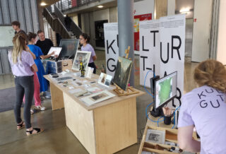 Eine Gruppe von Menschen steht um einen Tisch mit Kunst und Bildern.