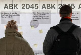 Zwei Personen stehen vor einer Wandtafel mit dem Titel 