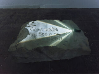 Eine Taschenlampe leuchtet auf eine große Steinplatte, auf deren Oberfläche die Worte 