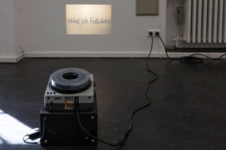 Ein Diaprojektor auf dem Boden projiziert den deutschen Text 