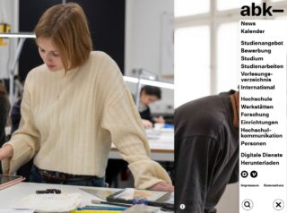 Eine junge Frau in einem cremefarbenen Pullover arbeitet an einem Tisch in einem Klassenzimmer oder Studio; auf der linken Seite ist ein Menü mit Optionen in deutscher Sprache zu sehen, darunter Nachrichten, Bewerbung und Studium.
