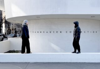 Zwei Personen in Winterkleidung stehen sich an einer niedrigen weißen Wand vor dem Gebäude der Sammlung Thannhauser gegenüber.