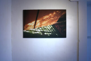 Ein Foto auf einer weißen Wand zeigt Sonnenlicht, das durch ein Fenster auf eine Oberfläche mit warmen und grünen Farbtönen fällt.