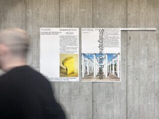 Eine Person mit kurzen Haaren geht an einer Betonwand vorbei, an der zwei Plakate mit Texten und Bildern zur 