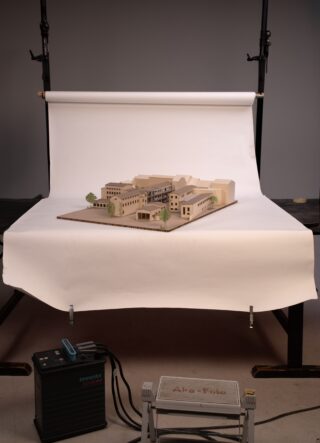Ein maßstabsgetreues Architekturmodell wird auf einem Tisch mit weißem Hintergrund in einem Fotostudio mit Beleuchtung, Ständern und elektrischer Ausrüstung ausgestellt.