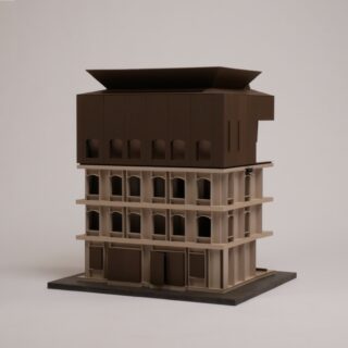 Ein maßstabsgetreues Architekturmodell mit einem beigen, mehrstöckigen Unterbau mit Bogenfenstern und einem dunkelbraunen, kastenförmigen Oberbau auf einer flachen Plattform.