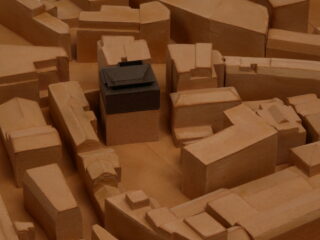 Ein architektonisches Tonmodell eines Stadtviertels mit einem dunklen Gebäude, das sich von hellen Strukturen abhebt.