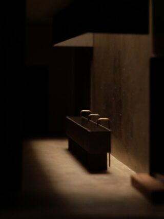 Ein schwach beleuchteter Flur mit einer langen Theke und drei Hockern an einer Wand, die Schatten auf den Boden werfen.