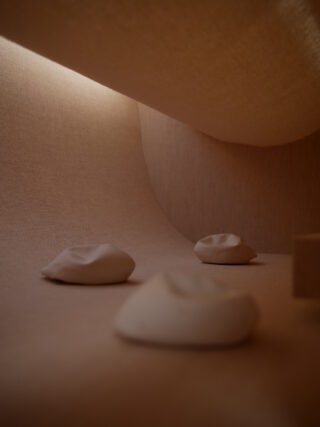 Drei glatte, abgerundete Steine ruhen auf einer weichen, beigefarbenen Oberfläche mit geschwungenen Wänden und diffuser Beleuchtung von oben.