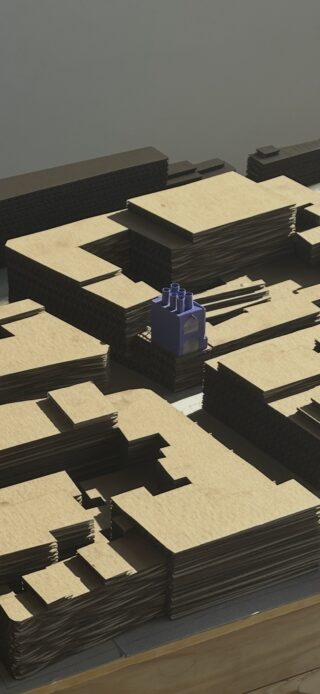 Stapel von zugeschnittenen Pappbögen mit einem kleinen violetten LEGO-ähnlichen Block oben auf einem Stapel unter direktem Sonnenlicht.