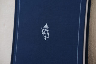 Nahaufnahme eines blauen strukturierten Bucheinbands mit einem kleinen weißen Blumenmuster in der Mitte und dünnen weißen Randlinien entlang der Kanten.