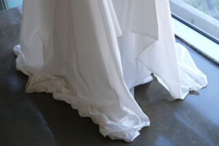 Eine Nahaufnahme des unteren Teils eines weißen Stoffkleides, das auf einem polierten Betonboden in der Nähe eines großen Fensters schwimmt.