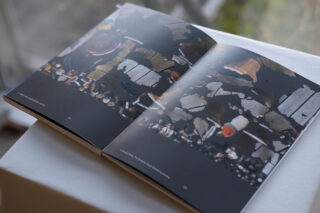 Ein aufgeschlagenes Buch auf einer weißen Fläche zeigt auf beiden Seiten abstrakte Bilder in dunklen und erdigen Tönen.