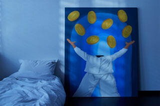 Ein großes Gemälde einer kopflosen Figur in Weiß mit erhobenen Armen, umgeben von schwebenden Goldmünzen, lehnt an einer blauen Wand neben einem ungemachten Bett.