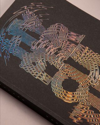 Nahaufnahme eines schwarzen Buches mit einem bunten, wellenförmigen, holografischen Linienmuster auf dem Einband vor einem neutralen Hintergrund.