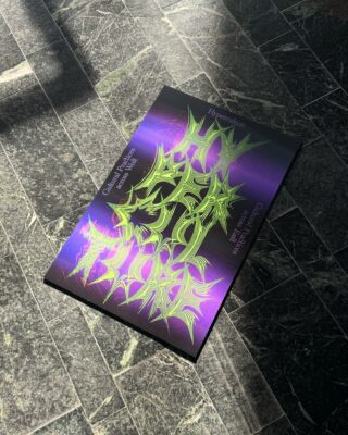 Eine Zeitschrift mit einem lila-grünen abstrakten Titelbild liegt auf einem dunklen Kachelboden, auf den das Sonnenlicht Schatten wirft.