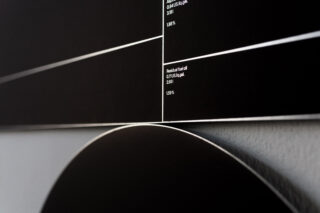 Nahaufnahme einer schwarzen und weißen geometrischen Wandgrafik mit dünnen weißen Linien, Textbeschriftungen und scharfen Winkeln.