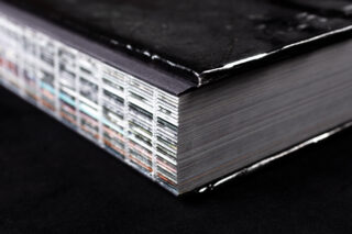 Eine Nahaufnahme der Ecke eines dicken Hardcover-Buches mit sichtbaren farbigen Seitenrändern, die auf einer schwarzen Oberfläche ruhen.