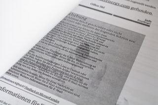 Nahaufnahme einer gedruckten Seite mit deutschem Text, teilweise verdeckt durch ein anderes Blatt Papier. Der Text scheint technisch zu sein, möglicherweise eine Anleitung zur Fehlerbehebung.