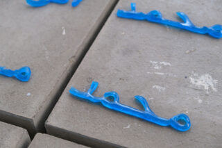 Blaue, verzweigte Glasobjekte liegen auf quadratischen Betonplatten mit sichtbaren Fugen und einigen weißen Flecken auf der Oberfläche.