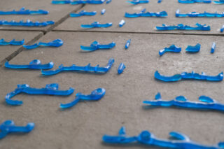 Blaue schriftzugartige Formen, die an Kalligraphie erinnern, sind auf großen grauen Bodenfliesen angeordnet.