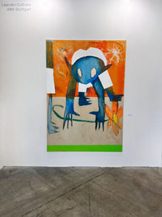 Ein großes, farbenfrohes Gemälde zeigt ein blaues Wesen mit langen Gliedmaßen und weißen Flecken vor einem orangefarbenen Hintergrund, das auf einer weißen Galeriewand ausgestellt ist.