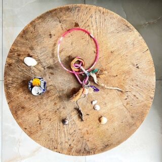 Ein runder Holztisch mit einer zerdrückten Fanta-Dose, einem rosafarbenen Plastikring, Schnur, Muscheln und kleinen sortierten Gegenständen, die darauf verstreut sind.