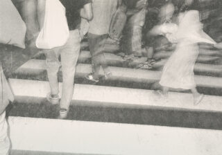 Menschen, die eine Straße an einem Zebrastreifen überqueren, einige von ihnen gehen zügig, mit unscharfen Bewegungen, die auf Bewegung in einer geschäftigen städtischen Umgebung hindeuten.