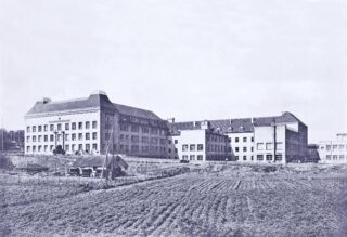 Historisches Schwarz-Weiß-Foto eines großen, mehrstöckigen Schulgebäudes mit der Aufschrift 