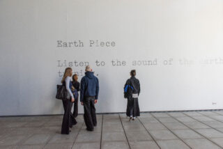 Vier Personen stehen vor einer weißen Wand mit der großen Aufschrift 