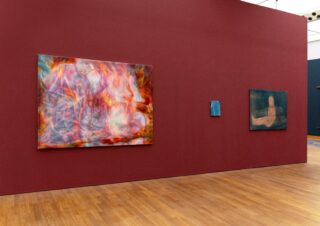 An einer kastanienbraunen Galeriewand mit Holzboden hängen drei abstrakte Gemälde; die Kunstwerke zeichnen sich durch vielfältige Farben und organische Formen aus.