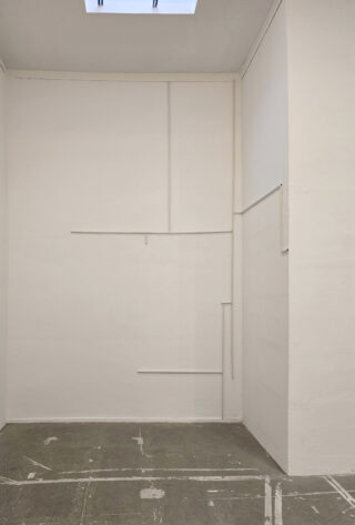 Ein minimalistischer weißer Raum mit einem Oberlicht, strukturierten Linien an der gegenüberliegenden Wand und einem abgenutzten Betonboden, der mit weißen Klebebandstreifen markiert ist.
