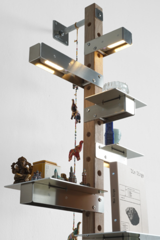 Ein modernes Regal mit Metallregalböden, die an einem Holzpfosten befestigt sind, auf denen kleine Dekoartikel, Figuren, Bücher und eine hängende Perlenkette ausgestellt sind.