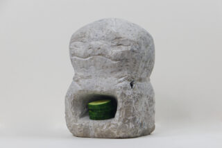 Eine Steinskulptur mit einer eingemeißelten Vertiefung, in der gestapelte Gurkenscheiben liegen, vor einem schlichten weißen Hintergrund.