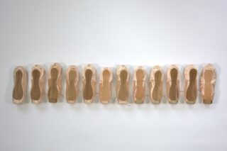 Zwölf Paar rosa Ballett-Spitzenschuhe sind in einer einzigen horizontalen Reihe vor einem schlichten weißen Hintergrund aufgereiht.