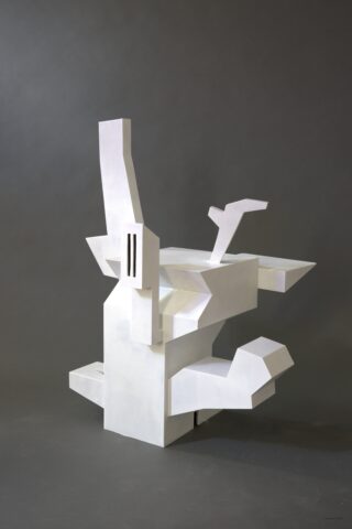 Weiße, abstrakte geometrische Skulptur mit kantigen Formen und Vorsprüngen vor einem schlichten dunkelgrauen Hintergrund.