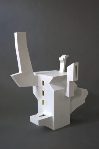 Weiße, abstrakte, geometrische Skulptur mit kantigen Vorsprüngen und drei kleinen, rechteckigen, gelben Öffnungen vor einem dunkelgrauen Hintergrund.