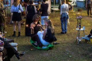 Zwei Frauen sitzen nachts draußen auf einem grünen Plastik-Teller-Schlitten, eine von ihnen hält eine brennende Wunderkerze in der Hand.