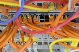 Ein Netzwerk-Switch, an dessen Anschlüsse zahlreiche orangefarbene, gelbe und blaue Ethernet-Kabel angeschlossen sind.