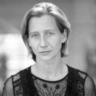 Schwarz-Weiß-Porträtfoto einer Frau, die direkt in die Kamera blickt.