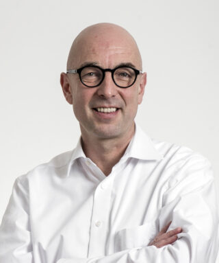 Ein lächelnder, kahlköpfiger Mann mit Brille und einem weißen Hemd.