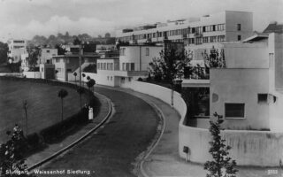 Schwarz-Weiß-Fotografie von Häusern im modernistischen Stil entlang einer geschwungenen Straße in der Weißenhofsiedlung in Stuttgart.